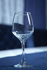 Tableware on table in cafe, focus on wineglass stem . Elegant table setting . Bakal blue background . Empty wine glass.