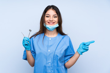 Woman dentist holding tools over isolated blue background pointing finger to the side