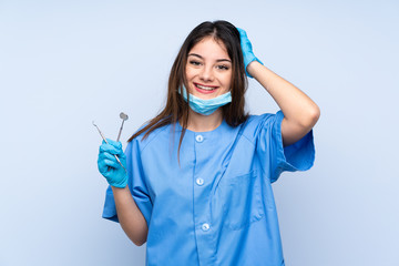 Woman dentist holding tools over isolated blue background laughing