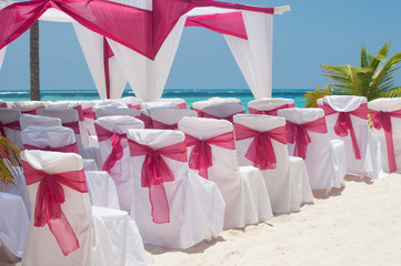 Beautiful outdoor wedding on beach scene: white chairs and arch decorated with red ribbon