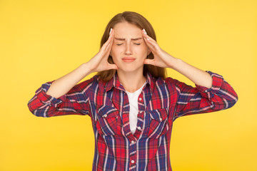 Headache. Portrait of stressed girl in checkered shirt clasping hands over sore head, grimacing from sudden pain having migraine, fever and flu symptoms. studio shot isolated on yellow background