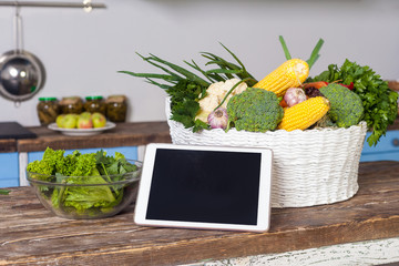Tablet pc, fresh vegetables and cooked salad on wooden table in modern kitchen, concept of online...