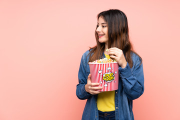 Young brunette woman over isolated pink background holding a big bucket of popcorns