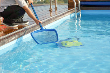 Hotel staff worker cleaning the pool. Pool cleaner during his work. Cleaning robot for cleaning the botton of swimming pools. 