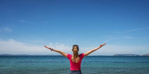 Obraz premium Young woman celebrating life with her arms spread widely, standing by the sea