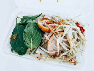 Sprouts, herbs, sausage on top of rice paper in a white styrofoam box