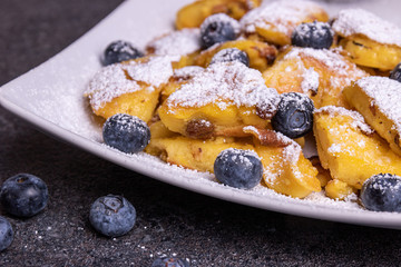Kaiserschmarrn, traditional austrian cut-up and sugared pancake with fruits on a white plate