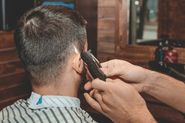 Haircut at the hairdresser. Barber cuts the hair on the client's head. The process of creating hairstyles for men. A man in a barbershop. The near plan. Equipment stylist. Selective focus