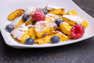 Kaiserschmarrn, traditional austrian cut-up and sugared pancake with fruits on a white plate