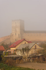 Old houses on the background of a medieval castle in the fog. Ukraine