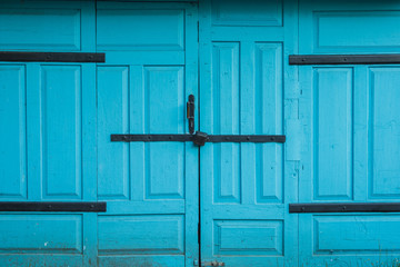 Closed garage doors of blue color with an old hinged lock