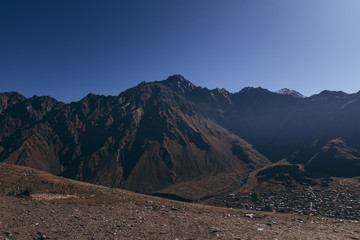stylish bearded man with camera in hands on top of Georgian mountains: nature photographer traveler taking photo of beautiful landscape from top of the mountain