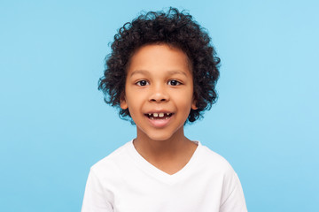 Closeup portrait of amazing cheerful little boy with curly hairdo in white T-shirt looking at...