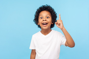 Eureka! Portrait of smart little boy with curly hair pointing finger up and looking inspired by genius thought, showing good idea sign, having clever solution in mind. studio shot blue background - obrazy, fototapety, plakaty
