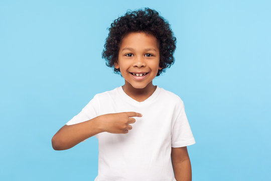 This Is Me. Portrait Of Happy Preschool Curly Boy In T-shirt Joyfully Looking At Camera And Pointing To Himself, Proud Of Own Success, Egoistic Child. Indoor Studio Shot Isolated On Blue Background