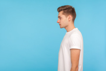 Profile of young serious guy with stylish hairdo in casual white t-shirt standing, looking to the...
