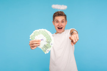 Portrait of surprised happy angelic man in t-shirt and with halo over head holding euro banknotes...