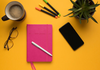 Stock photo of a diary with pencil and smartphone on a yellow background