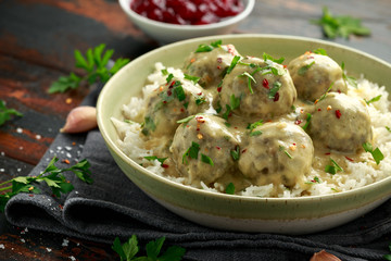 Hot Swedish meatballs with white rice and cranberry sauce on wooden table