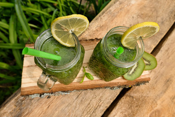 Two cans of homemade smoothies of green vegetables and fruits on a wooden table in the summer garden. Refreshing smoothie-diet dish, veganism, healthy eating, fitness.