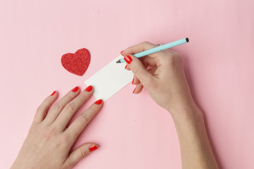 Top view of female writing a note on a pink background, Valentine's day, Mother's day, holiday concept