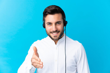 Telemarketer man working with a headset over isolated blue background handshaking after good deal