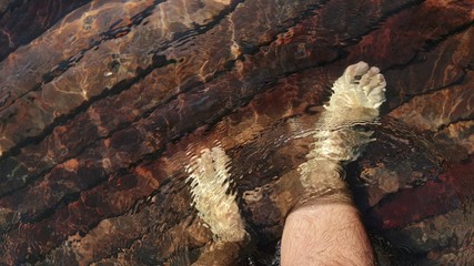 Naked hairy male legs walk on pier. The legs of a man swim. First person of view. Men rest on a flood wood underwater pier.