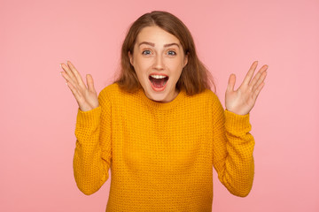 Wow, oh my god! Portrait of amazed excited ginger girl in sweater raising hands and looking at camera with astonishment, shocked by unexpected success. indoor studio shot isolated on pink background