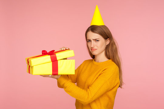 Portrait Of Unhappy Ginger Girl With Part Cone On Head Opening Gift Box And Looking Sadly At Camera, Disappointed With Birthday Surprise, Bad Present And Spoiled Holidays. Studio Shot Pink Background