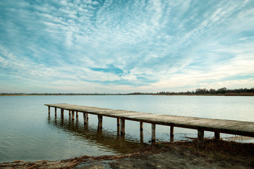 Fototapeta na wymiar A long wooden bridge on the water and cloudscape, Staw, Poland