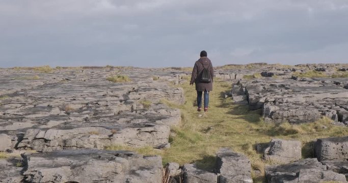 Wide shot of a woman walking over rocky terrain near Doolin on the Irish coast in cold weather.
