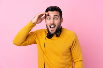 Young handsome man with earphones over isolated pink background with surprise and shocked facial expression