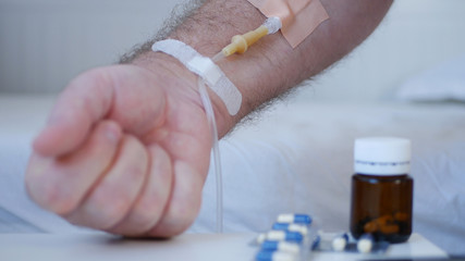 Suffering Man with a Medical Perfusion in Hand and Pills on the Table, Medical Emergency Services