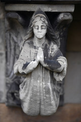 A weathered sandstone sculpture of a praying angel in front of a crypt on a cemetery in Berlin-Germany.