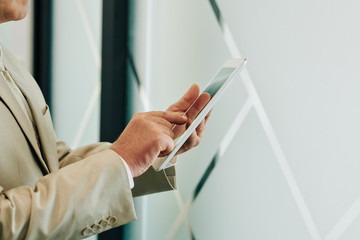 Unrecognzable man wearing beige suit using modern tablet PC, horizontal shot