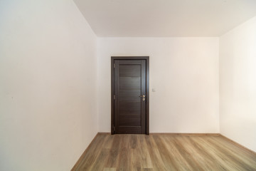 Closed wooden door in empty room, wooden flooring.  White walls