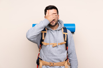 Young mountaineer man with a big backpack over isolated background covering eyes by hands