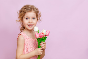 Cute little blonde girl with curly hair holding a bouquet of tulips. Studio portrait. Girl with tulips. Mother's day, March 8, international women's day.