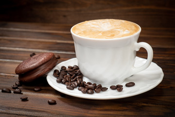 Cappuccino in a white glass with saucer. Coffee beans on a saucer and on a brown background. Nearby...
