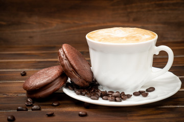 Cappuccino in a white glass with saucer. Coffee beans on a saucer and on a brown background. Nearby lies a chocolate cookie