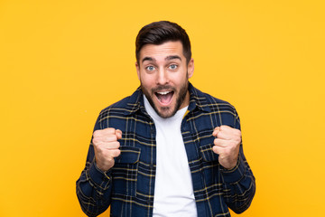 Young handsome man with beard over isolated yellow background celebrating a victory in winner position