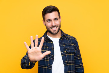 Young handsome man with beard over isolated yellow background counting five with fingers