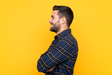 Fototapeta premium Young handsome man with beard over isolated yellow background in lateral position