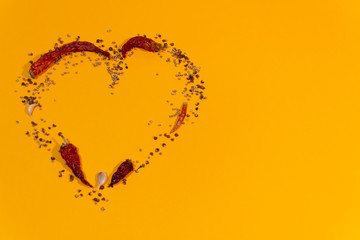 Heart mosaic of spices pepper, garlic, coriander on orange background with copy space