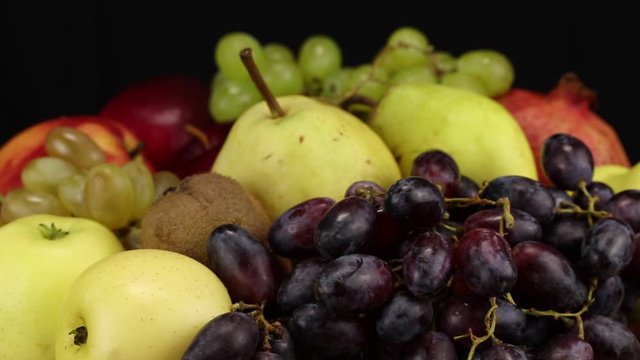 Dark grapes, yellow apples, kiwi and light grapes rotate counterclockwise, side view