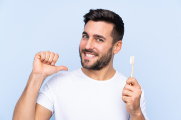 Young handsome man with beard brushing his teeth over isolated background proud and self-satisfied