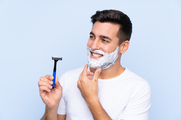 Young handsome man shaving his beard over isolated background looking side