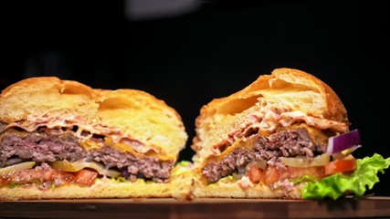 Cut craft burger is cooking on black background. Consist: sauce, lettuce, tomato, red onion, pickle, cheese, bacon, air bun and marbled meat beef.