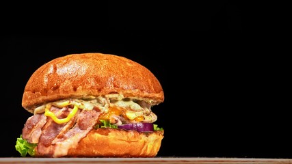 Craft burger is cooking on black background. Consist: sauce, lettuce, tomato, red onion, cucumber, cheese, bacon, air bun and breast of chicken.