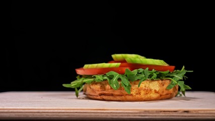 Craft burger is cooking on black background. Consist: sauce, arugula, tomato, red onion rings fries, cucumber, cheese, air bun and marble meat beef.